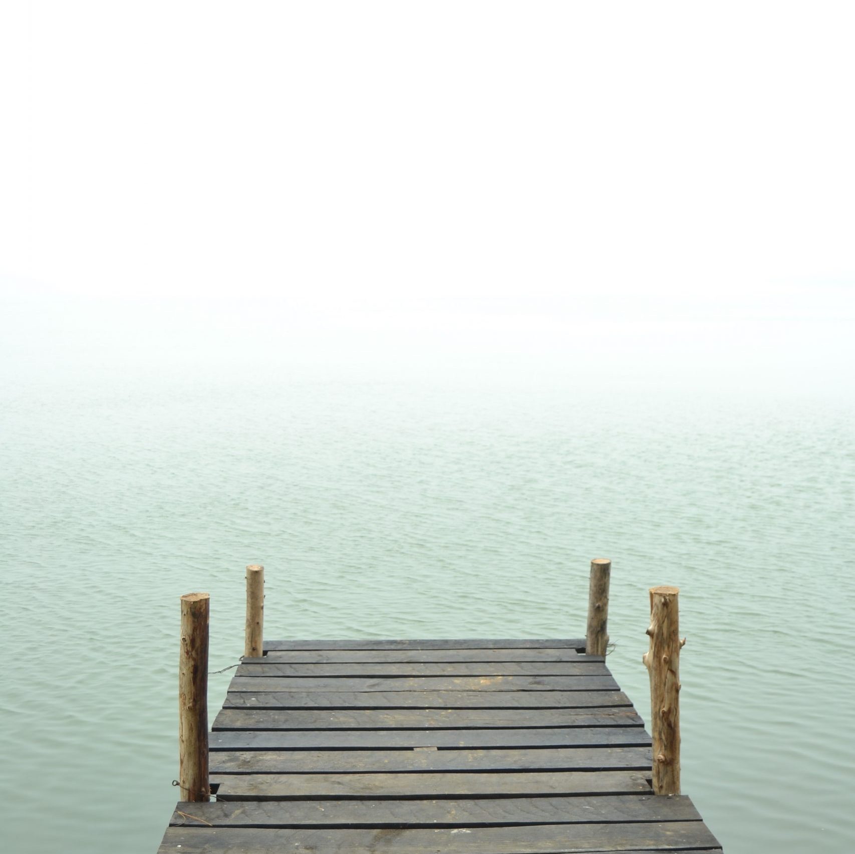 Ein Steg im Wasser, die Ferne verschwindet im Nebel